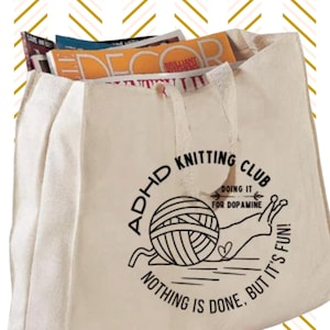 May include: A white canvas tote bag with a black graphic of a snail carrying a ball of yarn. The graphic includes the text "ADHD Knitting Club" and "Doing it for Dopamine. Nothing is done, but it's fun!"