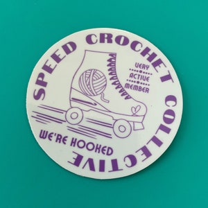 May include: A white round sticker with purple text that reads "Speed Crochet Collective" and "We're Hooked". The sticker features a purple line drawing of a roller skate with a ball of yarn in the skate.