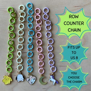May include: Five row counter chains for knitting, each featuring a series of colorful plastic rings linked by small metal jump rings. The chains are lime green, mint, blue, pink, and lavender, each ending with a unique charm: a yellow character, a white puppy, a white bear, a green moon, and a unicorn.
