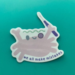 May include: A pink cartoon crab with a purple button eye and a needle and thread in its claw. The crab is on a white background with the text "we all make mistakes".