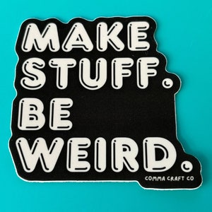 May include: Black and white sticker with the text "MAKE STUFF. BE WEIRD." in a bold, outlined font. The sticker has a white border and the text "COMMA CRAFT CO" in a smaller font at the bottom.