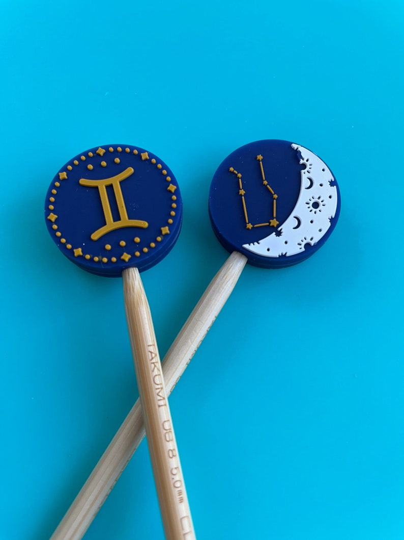 May include: Two wooden knitting needles with blue and gold Gemini and constellation designs on the ends. The needles are labelled "TAKUMI US 8 5.00 mm".