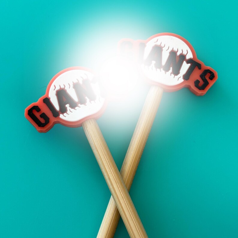 May include: Two wooden baseball bats with red and white baseball-shaped tops. The tops have the word "Giants" written on them in black.