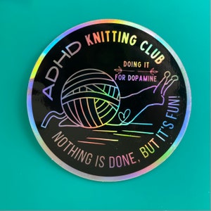 May include: A black and white sticker with a rainbow iridescent finish. The sticker features a snail carrying a ball of yarn and the text "ADHD Knitting Club Doing it for Dopamine Nothing is done, but it's fun!"