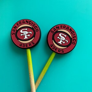 May include: Two red, white, and black San Francisco 49ers logo keychains with a stick attached to each.