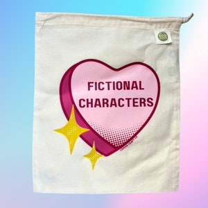 May include: A white cotton tote bag with a pink heart-shaped design that says "Fictional Characters" in red letters. The heart has a white polka dot pattern and is surrounded by two yellow stars.