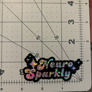 Op de afbeelding: Een zwarte en iriserende glitter sticker met de tekst "Neuro Sparkly" in een retro lettertype.