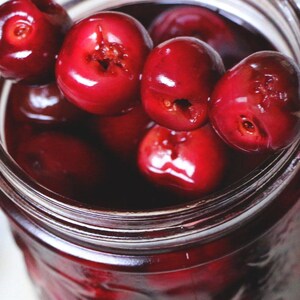 May include: A glass jar filled with red cherries in a sweet syrup. The cherries are arranged in a circular pattern, with the stems facing outward.