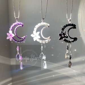 May include: Three crescent moon necklaces with crystal accents. The moons are made of wire wrapped with beads in purple, white, and black. Each necklace has a flower charm and crystal drops.