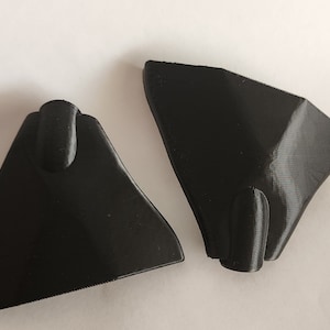 Puede incluir: Dos piezas de plástico negro, posiblemente partes de un juguete o modelo, con una superficie lisa y ligeramente texturizada.