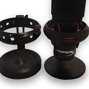 May include: Two black microphone stands. One is a circular holder with holes. The other has a black microphone with red accents and the word "HYPERX".