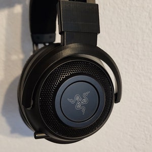 May include: Black Razer headphones with a black mesh speaker grill and a Razer logo on the front. The headphones have a black headband and earcups.