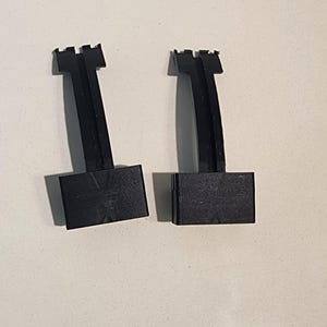 May include: Two black plastic clips with a square base and a curved top. The clips are designed to hold items together.