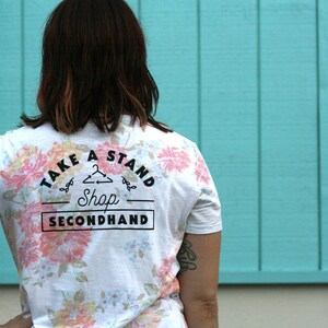 May include: A white t-shirt with a floral print and the text "Take a Stand Shop Secondhand" on the back.