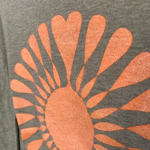 May include: A gray t-shirt with a large orange sun graphic. The sun is made up of a circle with radiating lines that resemble petals.