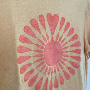 May include: A yellow t-shirt with a pink sunburst design. The sunburst is made up of a circle of pink hearts.