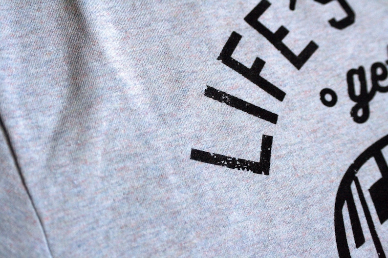 Op de afbeelding: Grijs T-shirt met zwarte tekst die "Life's a journey, get lost." luidt.