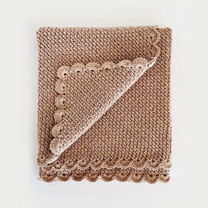 Op de afbeelding: Een gehaakt babydekentje in een lichtbruine kleur met een gegolfde rand.