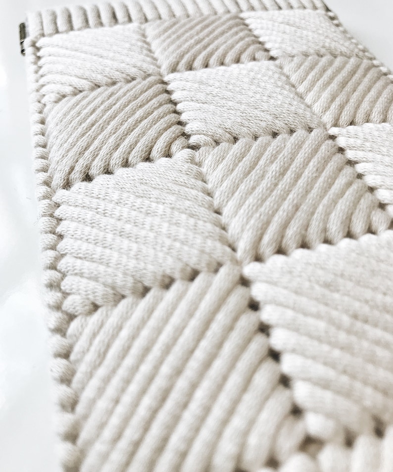 May include: A close-up of a white woven wall hanging with a diamond pattern. The hanging is made of thick, textured rope and has a simple, modern design.