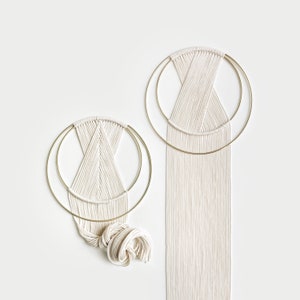 May include: Two macrame wall hangings with circular gold hoops and white yarn. The larger hanging has a long fringe of white yarn.