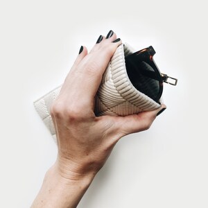May include: A hand holding a white quilted glasses case with a pair of brown and black sunglasses inside.