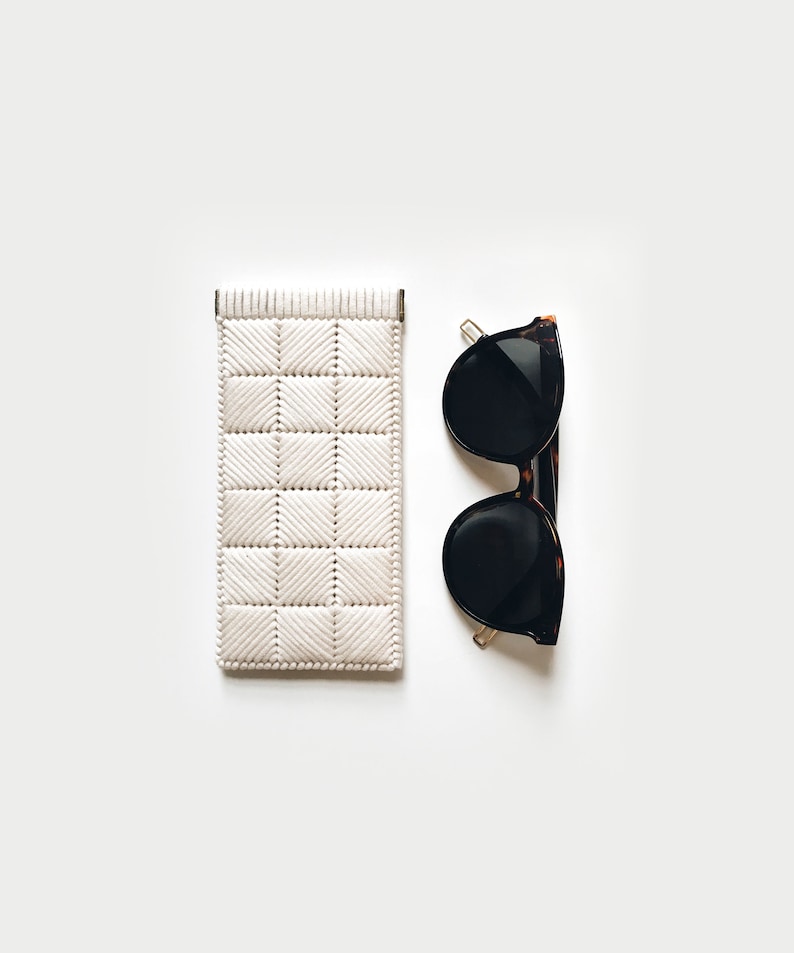 May include: A white woven sunglasses case and a pair of black sunglasses with tortoise shell frames.