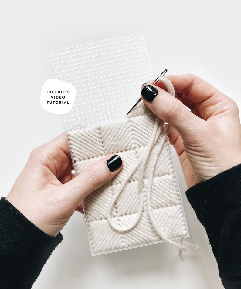 May include: A close-up of a person's hands working on a white yarn project on a plastic grid. The yarn is woven in a herringbone pattern. The image includes the text "Includes Video Tutorial".