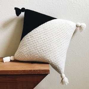 Peut inclure: Un oreiller blanc et noir avec des pompons. L'oreiller est fait d'un tissu doux et texturé et présente un motif géométrique.
