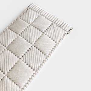 May include: A white woven watch band with a diamond pattern. The band is made of a soft, flexible material and has a secure clasp.