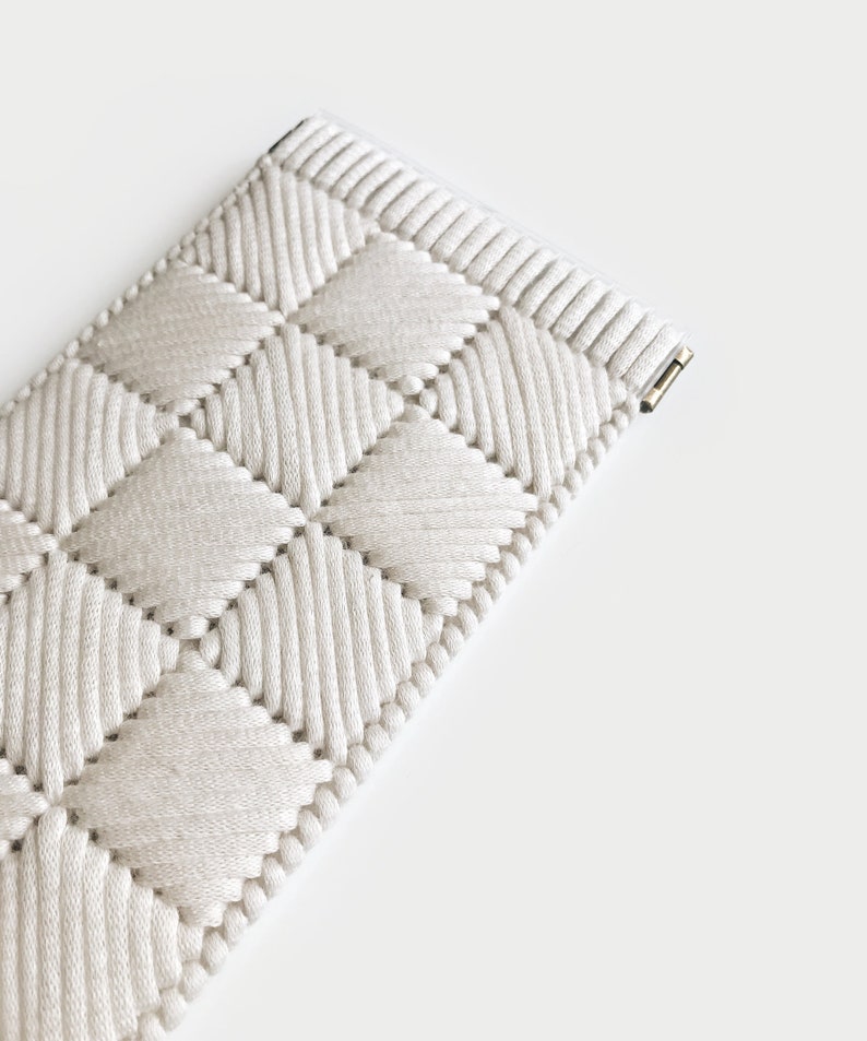 May include: A white woven watch band with a diamond pattern. The band is made of a soft, flexible material and has a secure clasp.