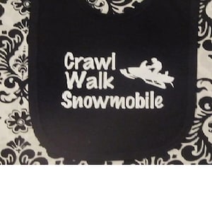 May include: Black bib with white embroidery that reads "Crawl Walk Snowmobile" and a white silhouette of a snowmobile.