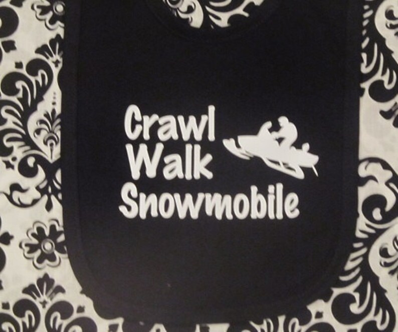 May include: Black bib with white text that reads "Crawl Walk Snowmobile" and a white silhouette of a snowmobile.