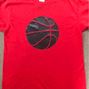 May include: Red t-shirt with a black basketball graphic.