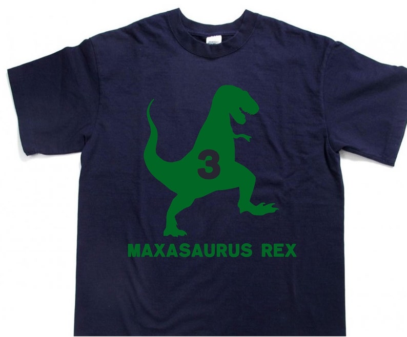 May include: A dark blue t-shirt with a green dinosaur silhouette and the number 3 inside the dinosaur. The text "MAXASAURUS REX" is printed below the dinosaur.