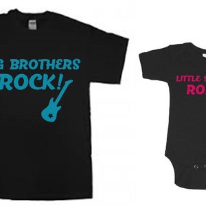 Puede incluir: Dos camisetas negras con un gr&aacute;fico de guitarra y texto. La camiseta m&aacute;s grande dice "Big Brothers Rock!" en texto azul. La camiseta m&aacute;s peque&ntilde;a dice "Little Sisters Roll!" en texto rosa.