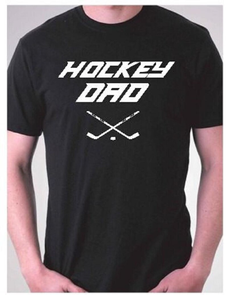 K&ouml;nnte beinhalten: Schwarzes T-Shirt mit wei&szlig;em Text "Hockey Dad" und einer Grafik von zwei gekreuzten Hockeyschl&auml;gern.