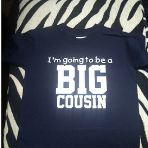 May include: A navy blue t-shirt with white text that reads "I'm going to be a BIG COUSIN".