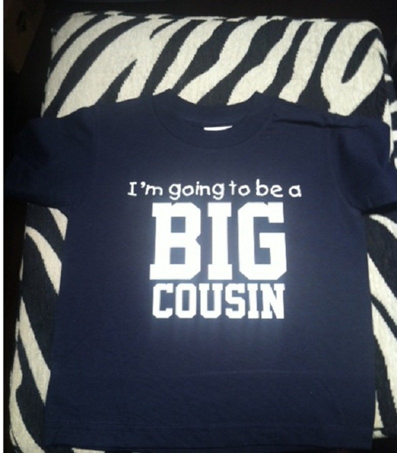 May include: A navy blue t-shirt with white text that reads "I'm going to be a BIG COUSIN".