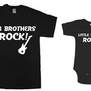 Puede incluir: Dos camisetas negras con un gr&aacute;fico de guitarra blanco y texto. La camiseta m&aacute;s grande dice "Big Brothers Rock!" y la camiseta m&aacute;s peque&ntilde;a dice "Little Sisters Roll!"