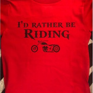 Op de afbeelding: Rood T-shirt met zwarte tekst die "I'd rather be riding" zegt en een zwart silhouet van een motorfiets.