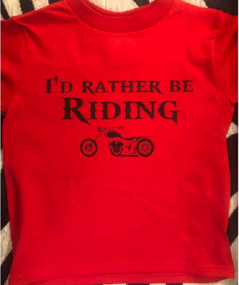 Op de afbeelding: Rood T-shirt met zwarte tekst die "I'd rather be riding" zegt en een zwart silhouet van een motorfiets.