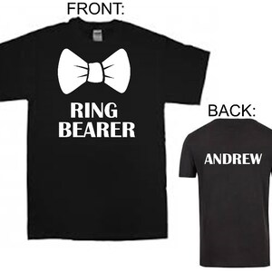 Puede incluir: Camiseta negra con una pajarita blanca y el texto "RING BEARER". La parte posterior de la camiseta tiene el nombre "ANDREW" impreso en blanco.