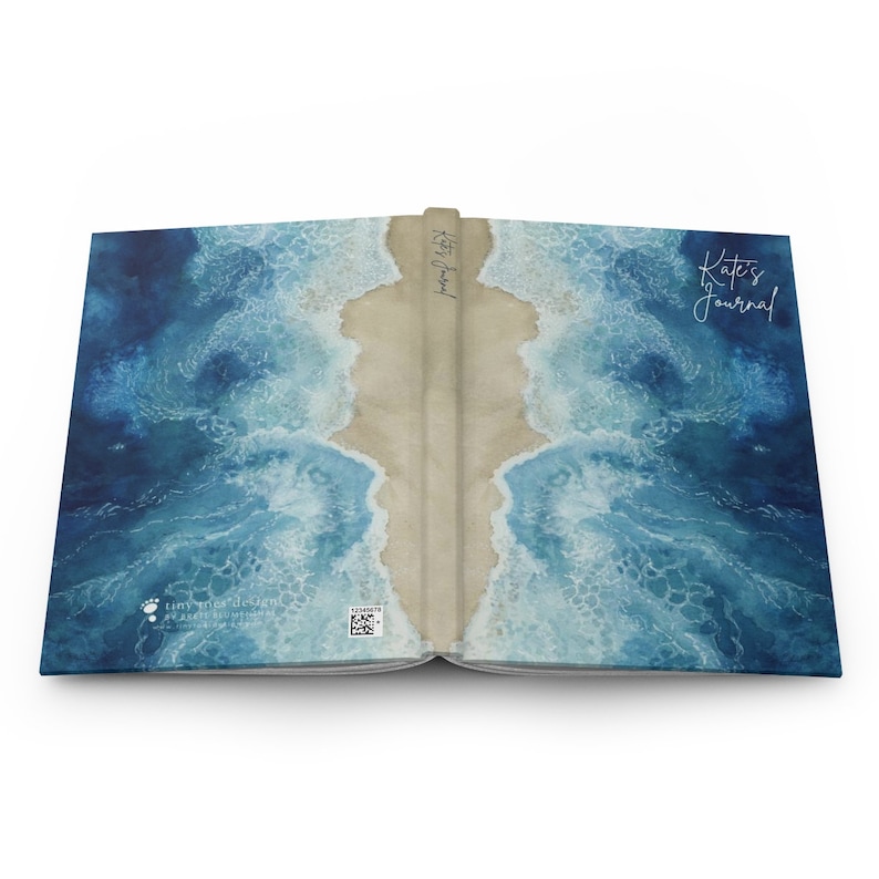 May include: A blue and brown journal with a watercolor design of ocean waves crashing on a sandy beach. The front cover has the text "Kate's Journal" in white cursive writing. The back cover has a small logo and a QR code.