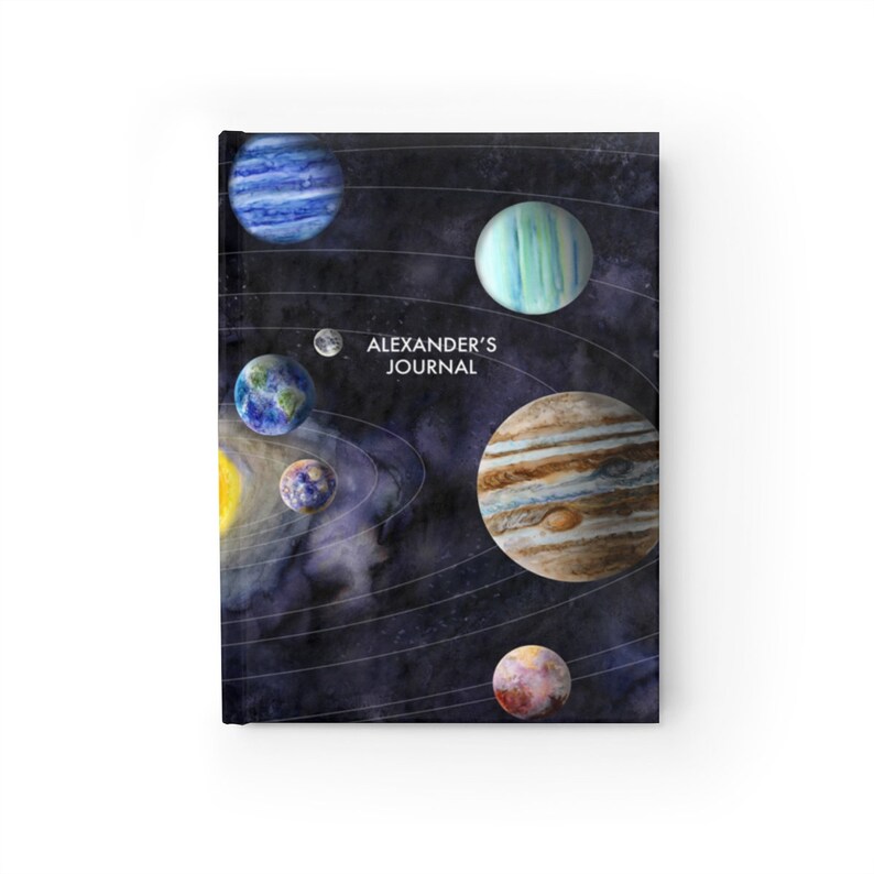 May include: A black journal featuring a watercolour illustration of planets in a solar system. The text "ALEXANDER'S JOURNAL" is printed on the cover.