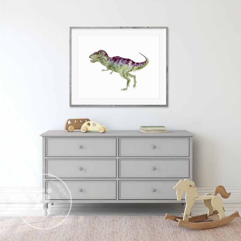 Pode incluir: Uma pintura em aquarela de um dinossauro verde e roxo em uma moldura branca pendurada em uma parede branca acima de uma c&ocirc;moda cinza com seis gavetas. H&aacute; dois carrinhos de brinquedo de madeira no topo da c&ocirc;moda e um cavalinho de balan&ccedil;o de madeira na frente da c&ocirc;moda.