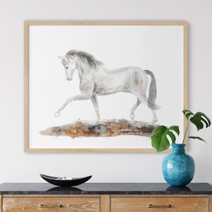 May include: A watercolor painting of a white horse running on a brown and orange background. The horse is in mid-stride with its legs extended. The painting is framed in a light wood frame.