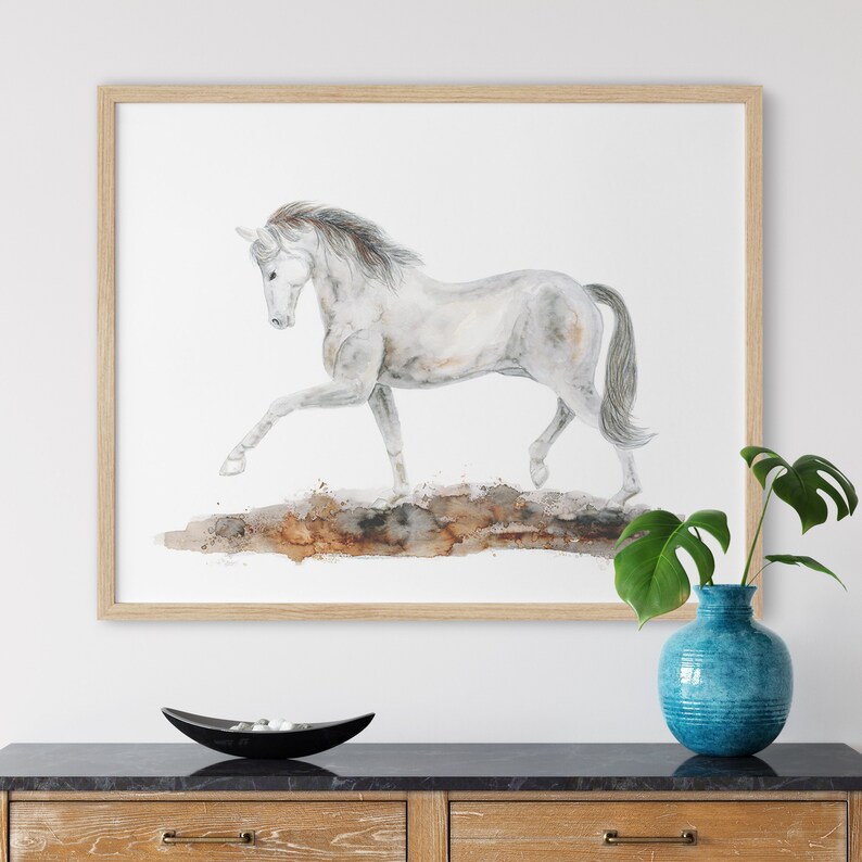 May include: A watercolor painting of a white horse running on a brown and orange background. The horse is in mid-stride with its legs extended. The painting is framed in a light wood frame.