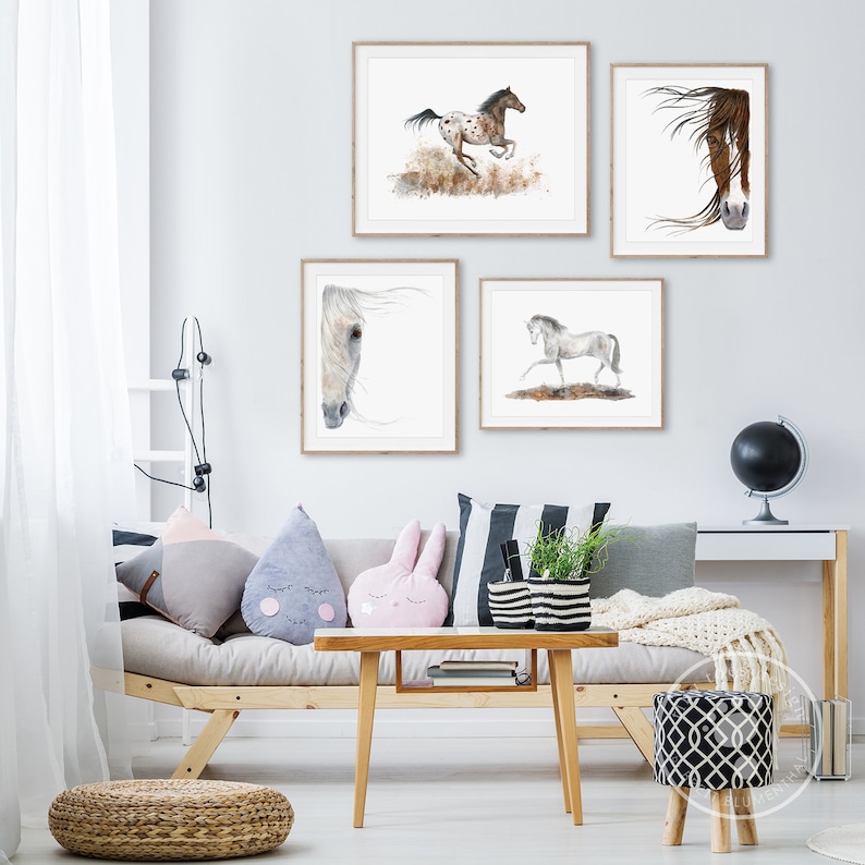 May include: Four framed watercolour paintings of horses in a living room setting. The paintings are hung on a white wall above a light brown sofa with cushions. The sofa is in front of a coffee table with a plant in a black and white striped planter. There is a small stool with a black and white pattern in the lower right corner of the image.