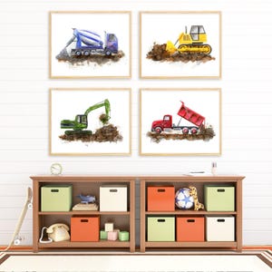 May include: Four framed watercolour prints featuring construction vehicles: a blue cement mixer, a yellow bulldozer, a green excavator, and a red dump truck. Each vehicle is depicted working on a pile of dirt against a plain white background.