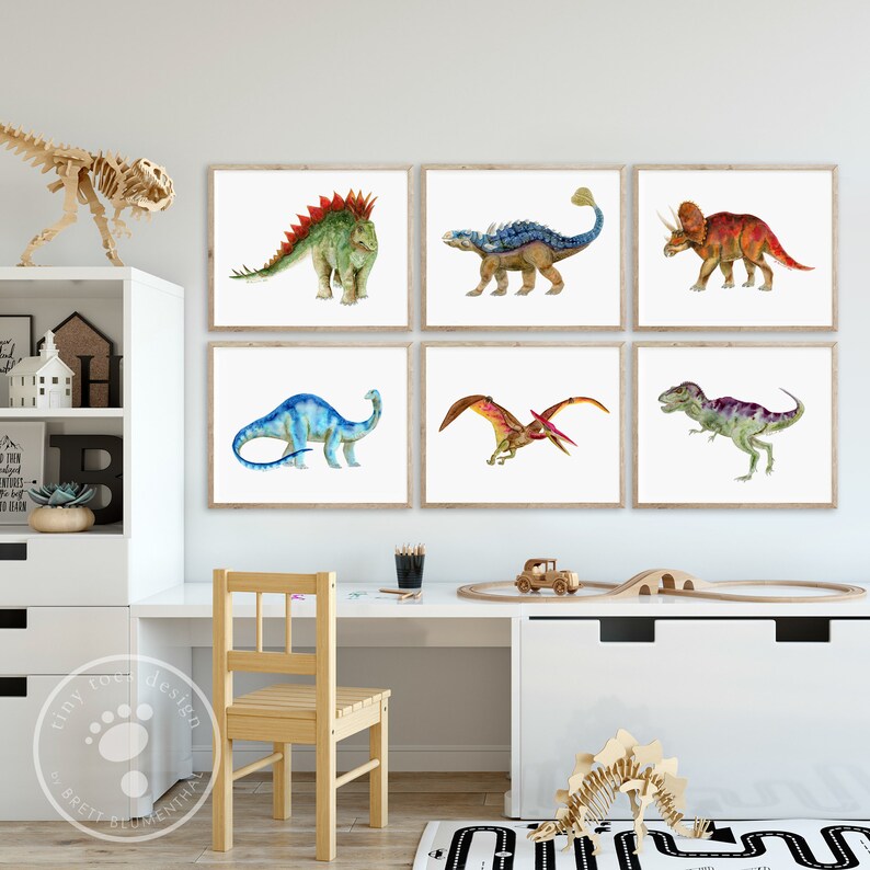 Pode incluir: Seis impress&otilde;es de dinossauros em aquarela emolduradas em um quarto infantil. As impress&otilde;es apresentam uma variedade de dinossauros, incluindo um estegossauro, um tricer&aacute;topo, um pterod&aacute;ctilo e um tiranossauro rex. As impress&otilde;es est&atilde;o penduradas em uma parede branca acima de uma mesa e uma cadeira brancas.